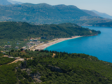 Aerial view of the turquoise waters and sandy shoreline of Aquarium Beach nestled between lush green hills and rugged mountains in Jala Vlore County Albania. Aerial view of the turquoise waters and sandy shoreline of Aquarium Beach nestled between lush green hills and rugged mountains in Jala Vlore County Albania.