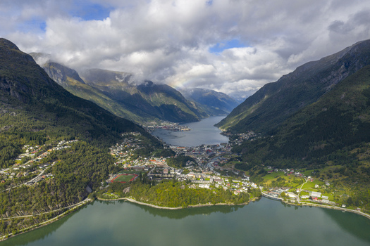 Aerial view of the town of Odda situated between the lake and the fjord surrounded by steep mountains with a rainbow in the clouds Odda Vestland Norway. Aerial view of the town of Odda situated between the lake and the fjord surrounded by steep mountains with a rainbow in the clouds Odda Vestland Norway.