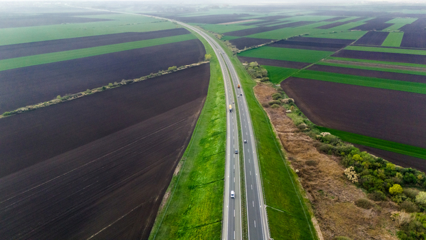 Aerial view of a ribbon of highway stretches through the vivid patchwork of agricultural fields a contrast of dark earth and vibrant green Sremska Mitrovica Vojvodina Serbia. Aerial view of a ribbon of highway stretches through the vivid patchwork of agricultural fields a contrast of dark earth and vibrant green Sremska Mitrovica Vojvodina Serbia.