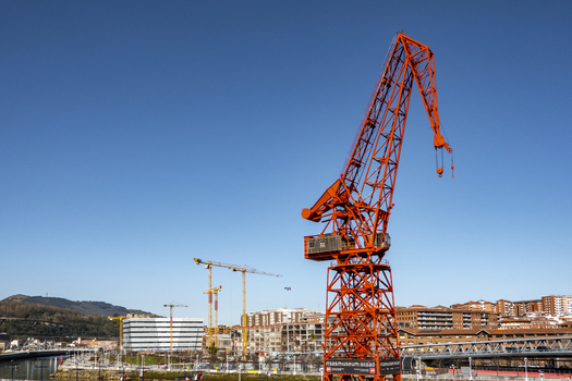 View of the iconic red Carola Crane at the Itsasmuseum Bilbao with urban buildings and a clear blue sky in Greater Bilbao Basque Country Spain. View of the iconic red Carola Crane at the Itsasmuseum Bilbao with urban buildings and a clear blue sky in Greater Bilbao Basque Country Spain.
