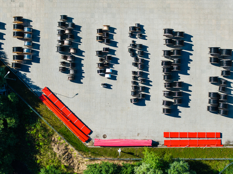 Aerial view of a warehouse storage area featuring rows of industrial cable spools and stacks of red pipes on a paved surface in Lielvarzi Kekava Municipality Latvia. Aerial view of a warehouse storage area featuring rows of industrial cable spools and stacks of red pipes on a paved surface in Lielvarzi Kekava Municipality Latvia.