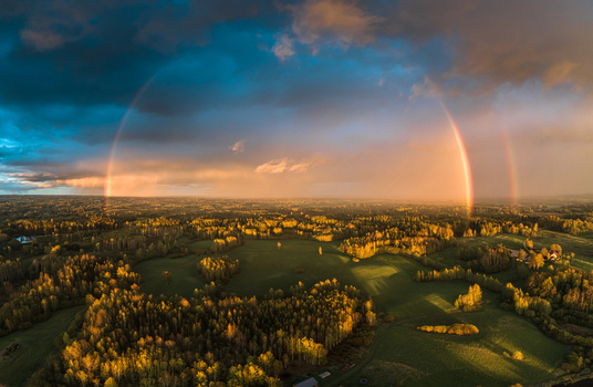 Aerial view of a double rainbow arching over the lush green forests and fields of Latvia. Aerial view of a double rainbow arching over the lush green forests and fields of Latvia.