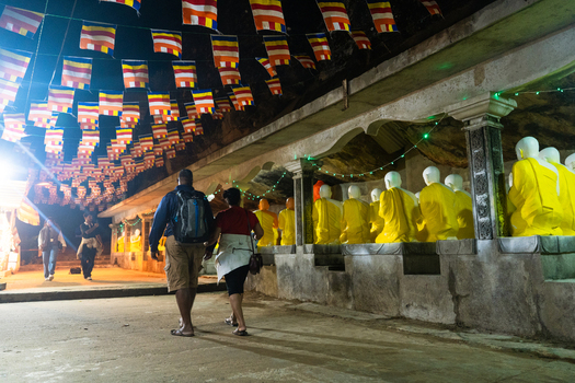 Ratnapura Sri Lanka 22 February 2026 View of pilgrims walking past rows of yellow Buddha statues under hanging Buddhist flags at Adam s Peak at night.