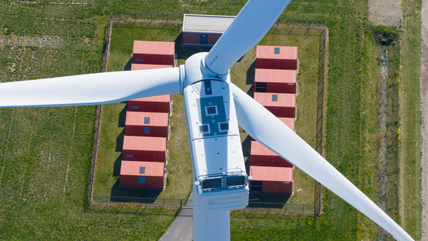 Aerial view of a wind turbine nacelle and blades above red shipping containers in a fenced enclosure Middelharnis South Holland Netherlands. Aerial view of a wind turbine nacelle and blades above red shipping containers in a fenced enclosure Middelharnis South Holland Netherlands.
