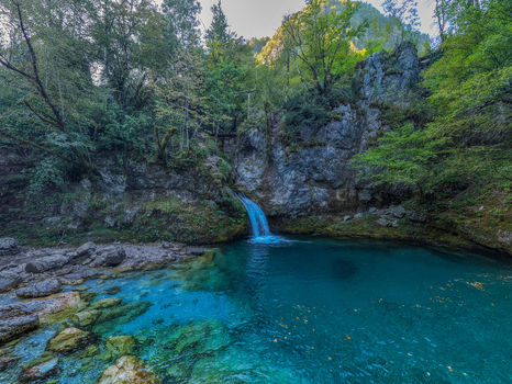 Aerial view of the Blue Eye Theth a natural spring with vibrant turquoise water flowing from a rocky cliff surrounded by lush green forest in Theth Shkoder County Albania. Aerial view of the Blue Eye Theth a natural spring with vibrant turquoise water flowing from a rocky cliff surrounded by lush green forest in Theth Shkoder County Albania.