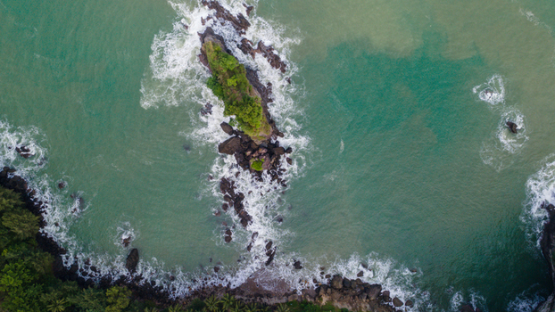 Aerial view of the rocky outcrop of Karang Agung Beach with lush green vegetation surrounded by turquoise sea water and crashing waves in Ayah Central Java Indonesia. Aerial view of the rocky outcrop of Karang Agung Beach with lush green vegetation surrounded by turquoise sea water and crashing waves in Ayah Central Java Indonesia.