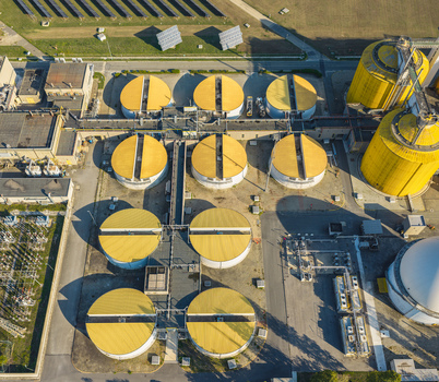 Aerial view of circular wastewater processing tanks with yellow roofs connected by pipelines beside solar panels at an industrial treatment facility in Italy. Aerial view of circular wastewater processing tanks with yellow roofs connected by pipelines beside solar panels at an industrial treatment facility in Italy.