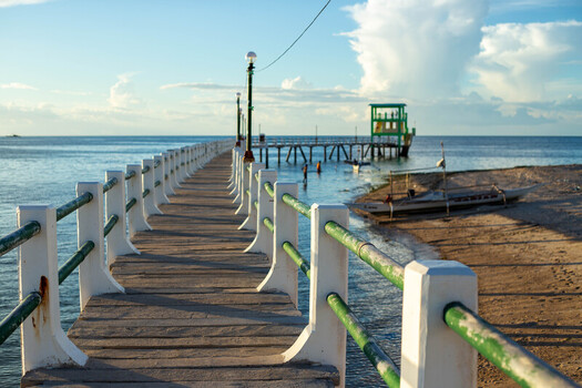 View of the wooden pier at Bantayan Island with green railings and white concrete posts extending into the calm sea under a clear blue sky in Cebu Central Visayas Philippines. View of the wooden pier at Bantayan Island with green railings and white concrete posts extending into the calm sea under a clear blue sky in Cebu Central Visayas Philippines.
