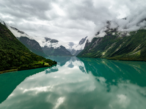 Aerial view of Lovatnet lake with turquoise water reflecting the surrounding steep mountains and green slopes under a cloudy sky in Stryn Municipality Vestland Norway.