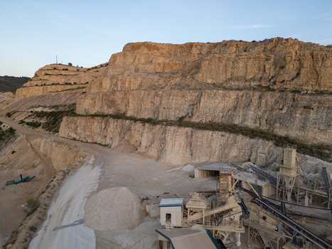 Aerial view of a limestone quarry with terraced rock faces industrial processing machinery and piles of gravel in Teulada Valencian Community Spain.