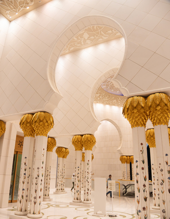 View of the ornate interior of the Sheikh Zayed Grand Mosque with white marble arches gold palm leaf columns and people walking Abu Dhabi Abu Dhabi United Arab Emirates. View of the ornate interior of the Sheikh Zayed Grand Mosque with white marble arches gold palm leaf columns and people walking Abu Dhabi Abu Dhabi United Arab Emirates.