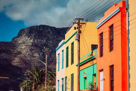 View of the vibrant colorful houses of Bo Kaap with the iconic Table Mountain rising in the background under a cloudy blue sky in Cape Town Western Cape South Africa. View of the vibrant colorful houses of Bo Kaap with the iconic Table Mountain rising in the background under a cloudy blue sky in Cape Town Western Cape South Africa.