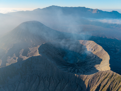 Aerial view of Mount Bromo crater with volcanic smoke rising from the rugged landscape in Tosari East Java Indonesia.