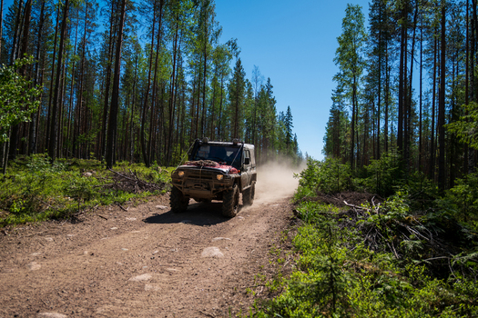 View of an off road vehicle driving on a dirt road through a pine forest near Lake Ladoga in Sortavala Respublika Kareliya Russia.