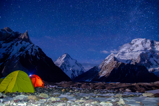 View of illuminated tents at base camp under a starry night sky with the snow capped peak of K2 in the background Skardu Gilgit Pakistan.