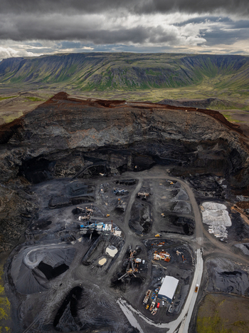 Aerial view of an open pit quarry with heavy machinery gravel piles and access roads set against a dramatic volcanic landscape under a cloudy sky in Iceland. Aerial view of an open pit quarry with heavy machinery gravel piles and access roads set against a dramatic volcanic landscape under a cloudy sky in Iceland.