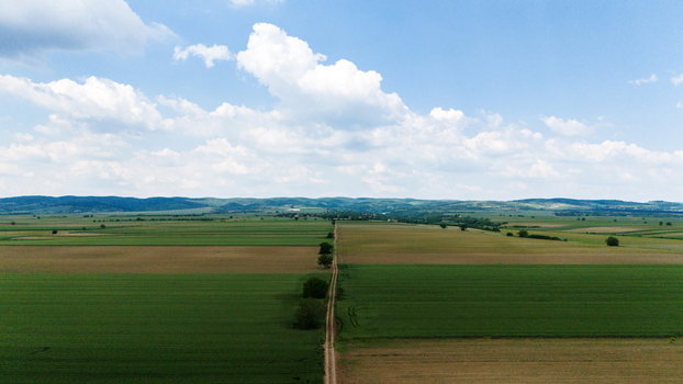 Aerial view of vast agricultural fields and a straight dirt road leading towards rolling hills under a cloudy sky Novi Sad Vojvodina Serbia. Aerial view of vast agricultural fields and a straight dirt road leading towards rolling hills under a cloudy sky Novi Sad Vojvodina Serbia.