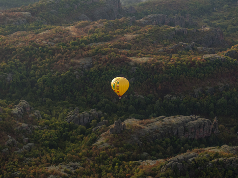 Aerial view of a yellow hot air balloon floating above the dramatic rock formations and dense forest of the Belogradchik Rocks in Belogradchik Vidin Bulgaria.