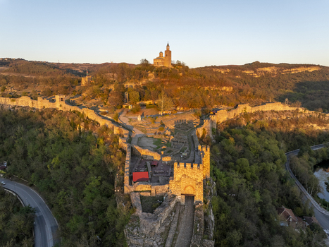 Aerial view of Tsarevets Fortress a historic medieval stronghold with stone walls and towers illuminated by golden light in Veliko Tarnovo Veliko Tarnovo Bulgaria. Aerial view of Tsarevets Fortress a historic medieval stronghold with stone walls and towers illuminated by golden light in Veliko Tarnovo Veliko Tarnovo Bulgaria.