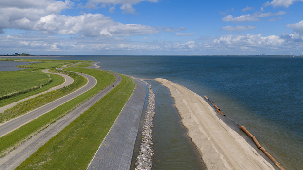 Aerial view of the dike reinforcement project along the coastline with a winding road green embankments and sandy construction works in Uitdam North Holland Netherlands.
