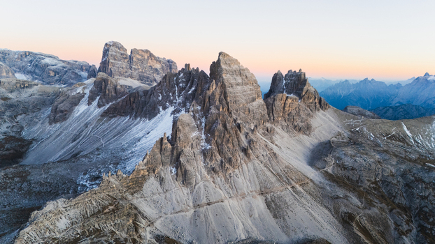 Aerial view of Tre Cime di Lavaredo with jagged peaks and snow dusted rocky slopes under a soft dawn sky Auronzo di Cadore Veneto Italy. Aerial view of Tre Cime di Lavaredo with jagged peaks and snow dusted rocky slopes under a soft dawn sky Auronzo di Cadore Veneto Italy.