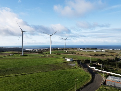 Aerial view of three wind turbines standing on green fields near a coastal town and the blue ocean under a cloudy sky Portugal. Aerial view of three wind turbines standing on green fields near a coastal town and the blue ocean under a cloudy sky Portugal.