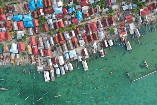 Aerial view of Pulau Maginti featuring a dense coastal settlement with colorful rooftops and small boats anchored in the clear turquoise water of Maginti South East Sulawesi Indonesia.