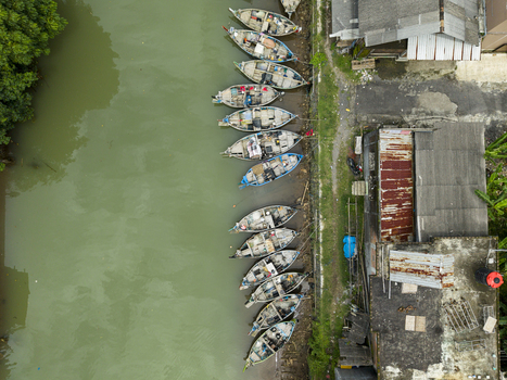 Aerial view of fishing boats resting along the riverbank creating a mosaic of colors and textures next to waterside buildings Jepara Central Java Indonesia.