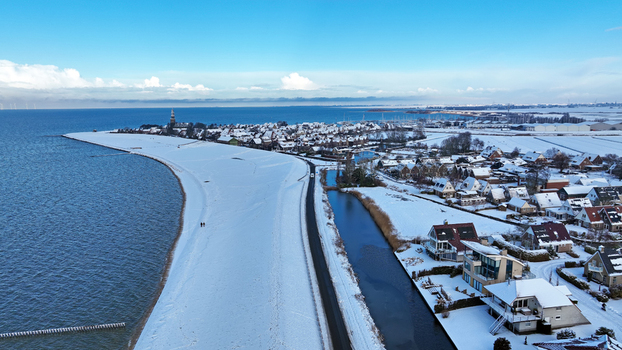 Aerial view of the snow covered coastal town of Hindeloopen with its historic rooftops a frozen canal and the dike along the IJsselmeer in Hindeloopen Friesland Netherlands. Aerial view of the snow covered coastal town of Hindeloopen with its historic rooftops a frozen canal and the dike along the IJsselmeer in Hindeloopen Friesland Netherlands.