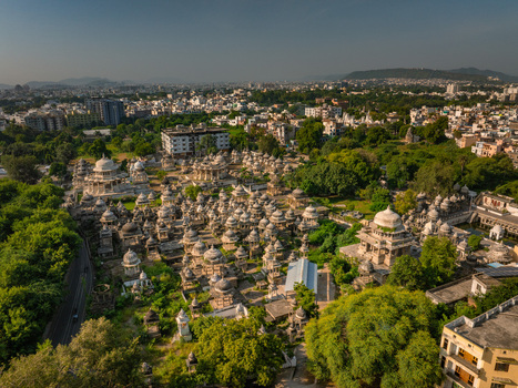 Aerial view of the historic Ahar Cenotaphs in Udaipur featuring numerous stone chhatris and domes surrounded by lush green trees and urban buildings in Udaipur Rajasthan India.