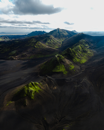 Aerial view of green moss clings to the dark volcanic slopes contrasting sharply with the somber earth under a vast sky Iceland. Aerial view of green moss clings to the dark volcanic slopes contrasting sharply with the somber earth under a vast sky Iceland.