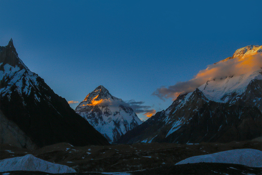 View of the high altitude K2 mountain peak illuminated by golden sunset light with surrounding snow capped ridges and glaciers under a clear blue sky in Skardu Gilgit Pakistan.