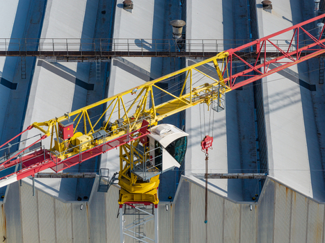 Aerial view of an agricultural machinery production facility with a large yellow and red construction crane positioned over industrial sawtooth roofs in Plock Mazowieckie Poland. Aerial view of an agricultural machinery production facility with a large yellow and red construction crane positioned over industrial sawtooth roofs in Plock Mazowieckie Poland.