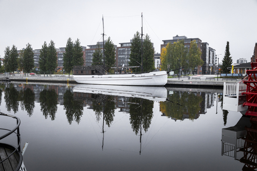 View of a white boat docked in the canal with reflections in the water and modern buildings in the background in Jyvaskyla Central Finland Finland.