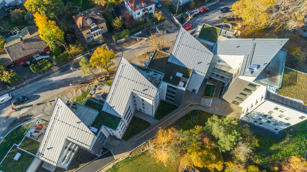 Aerial view of modern residential buildings with angular grey metal roofs and green terraces surrounded by autumn trees and a road in Sweden. Aerial view of modern residential buildings with angular grey metal roofs and green terraces surrounded by autumn trees and a road in Sweden.