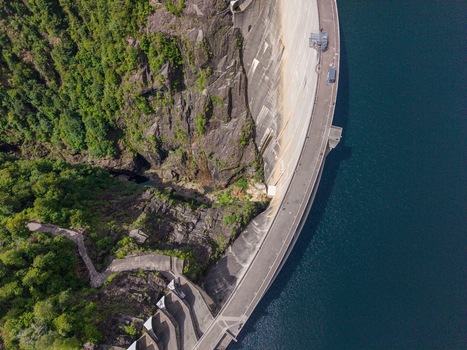 Aerial view of the massive curved concrete wall of the Verzasca Dam bordering deep blue water and steep rocky cliffs in Gordola Ticino Switzerland. Aerial view of the massive curved concrete wall of the Verzasca Dam bordering deep blue water and steep rocky cliffs in Gordola Ticino Switzerland.