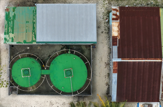 Aerial view of two large green storage tanks and industrial buildings with corrugated metal roofs in Hanimaadhoo Haa Dhaalu Atoll Maldives.