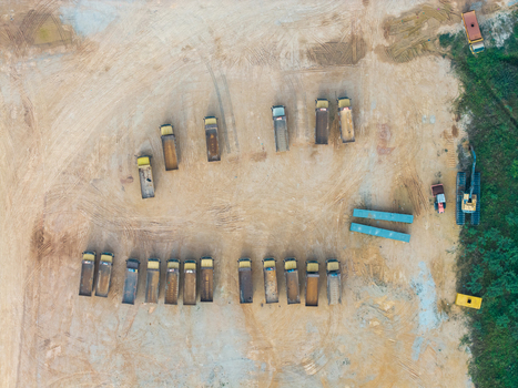 Aerial view of a construction area with rows of parked dump trucks and an excavator on dirt ground in Bukit Tambun Penang Malaysia. Aerial view of a construction area with rows of parked dump trucks and an excavator on dirt ground in Bukit Tambun Penang Malaysia.
