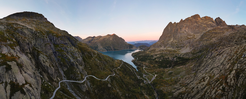 Aerial view of Barrage d Emosson reservoir surrounded by rugged alpine mountains and a winding road in the valley at sunset in Finhaut Valais Switzerland.