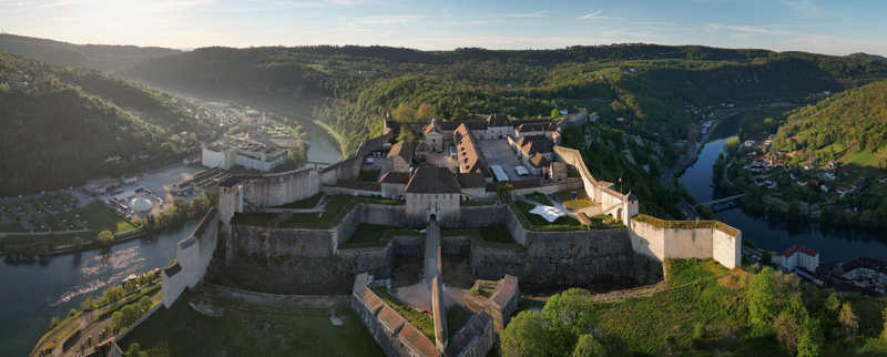 Aerial view of the Besancon Citadel overlooking the Doubs river loop and historic stone walls surrounded by lush green hills in Besancon Bourgogne Franche Comte France. Aerial view of the Besancon Citadel overlooking the Doubs river loop and historic stone walls surrounded by lush green hills in Besancon Bourgogne Franche Comte France.