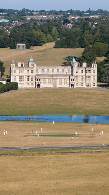 Aerial view of Audley End House surrounded by expansive parkland with a cricket match in progress on the lawn in Audley End England United Kingdom. Aerial view of Audley End House surrounded by expansive parkland with a cricket match in progress on the lawn in Audley End England United Kingdom.
