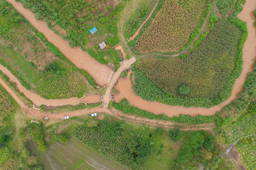 Aerial view of a muddy river flowing through agricultural fields and farmlands with a small bridge crossing the water in Butaleja Eastern Region Uganda. Aerial view of a muddy river flowing through agricultural fields and farmlands with a small bridge crossing the water in Butaleja Eastern Region Uganda.