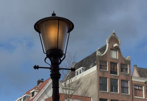 View of a vintage street lamp glowing warmly against the backdrop of old buildings and a cloudy sky Amsterdam North Holland Netherlands.