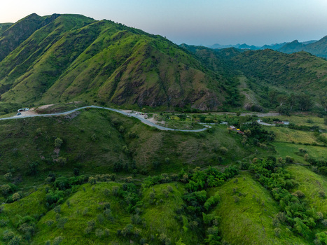 Aerial view of a winding road cutting through the lush green Aravalli hills under a soft sky in Udaipur Rajasthan India.