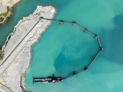 Aerial view of a gravel pit lake with a floating conveyor belt system and industrial machinery in the turquoise water surrounded by gravel banks in Aschheim Bavaria Germany.