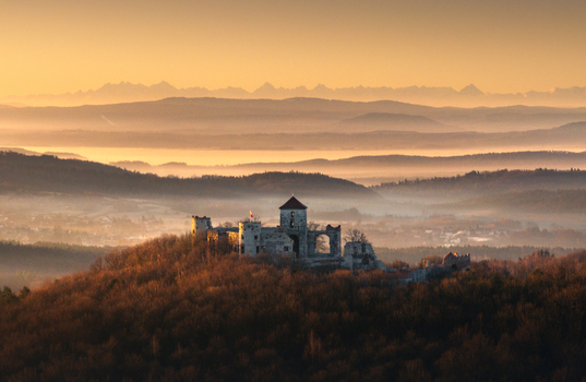 Aerial view of the medieval castle ruins on a forested hill in the Krakow Czestochowa Upland with morning mist and distant mountains Krakow County Lesser Poland Poland. Aerial view of the medieval castle ruins on a forested hill in the Krakow Czestochowa Upland with morning mist and distant mountains Krakow County Lesser Poland Poland.