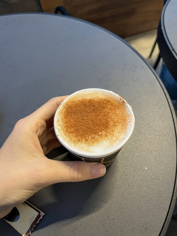 View of a hand holding a paper cup of coffee with cinnamon powder on top at a cafe table in Beylikduzu Istanbul Turkey. View of a hand holding a paper cup of coffee with cinnamon powder on top at a cafe table in Beylikduzu Istanbul Turkey.