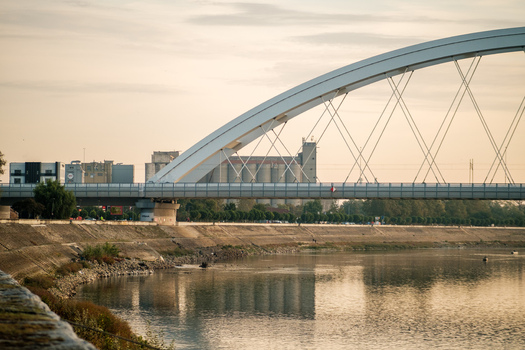 View of the Zezelj Bridge spanning the Danube River with industrial silos in the background under a soft evening light in Novi Sad Vojvodina Serbia. View of the Zezelj Bridge spanning the Danube River with industrial silos in the background under a soft evening light in Novi Sad Vojvodina Serbia.