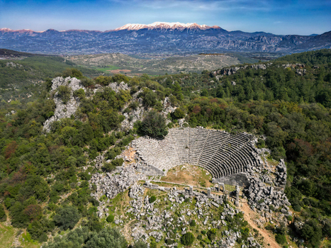 Aerial view of the ancient theater of Pinara nestled in a lush forest with snow capped mountains in the background in Pinararasi Mugla Turkiye.