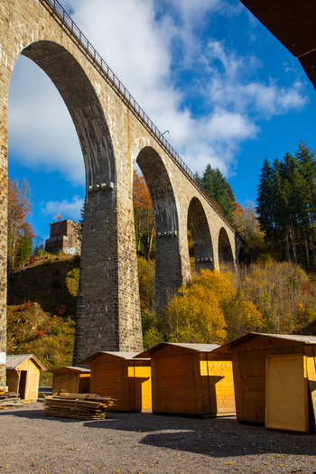 View of the Ravennaschlucht stone viaduct with autumn trees and small wooden huts under a blue sky in Breitnau Baden Wurttemberg Germany. View of the Ravennaschlucht stone viaduct with autumn trees and small wooden huts under a blue sky in Breitnau Baden Wurttemberg Germany.